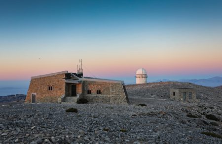 Pohled na správní budovu a kopuli 1,3m teleskopu, v pozadí pohoří Spathi s nejvyššími kopci kolem 2100 m n. m.