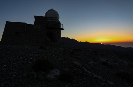 Západ Slunce s budovou 0,3m dalekohledu. Vpravo vedle kopule nejvyšší hora Kréty Psiloritis 2456 m n. m.